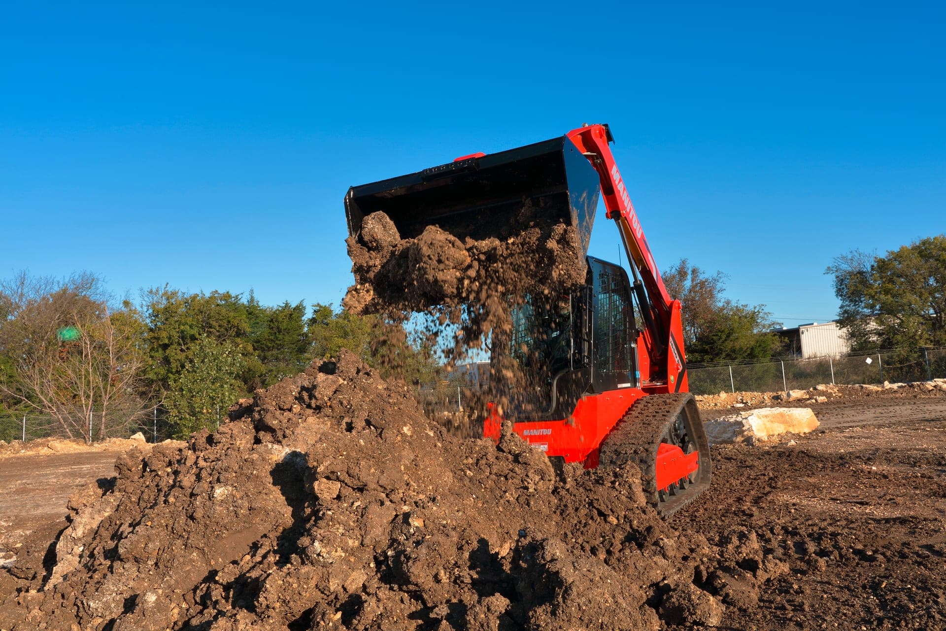 Manitou 1650 RT compact track loader dumping a bucket of dirt onto a jobsite pile